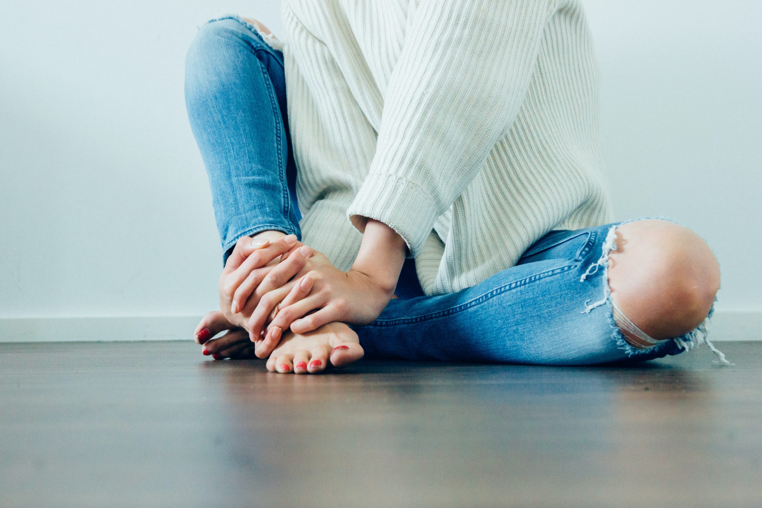 woman sitting on floor with ripped jeans and sweater